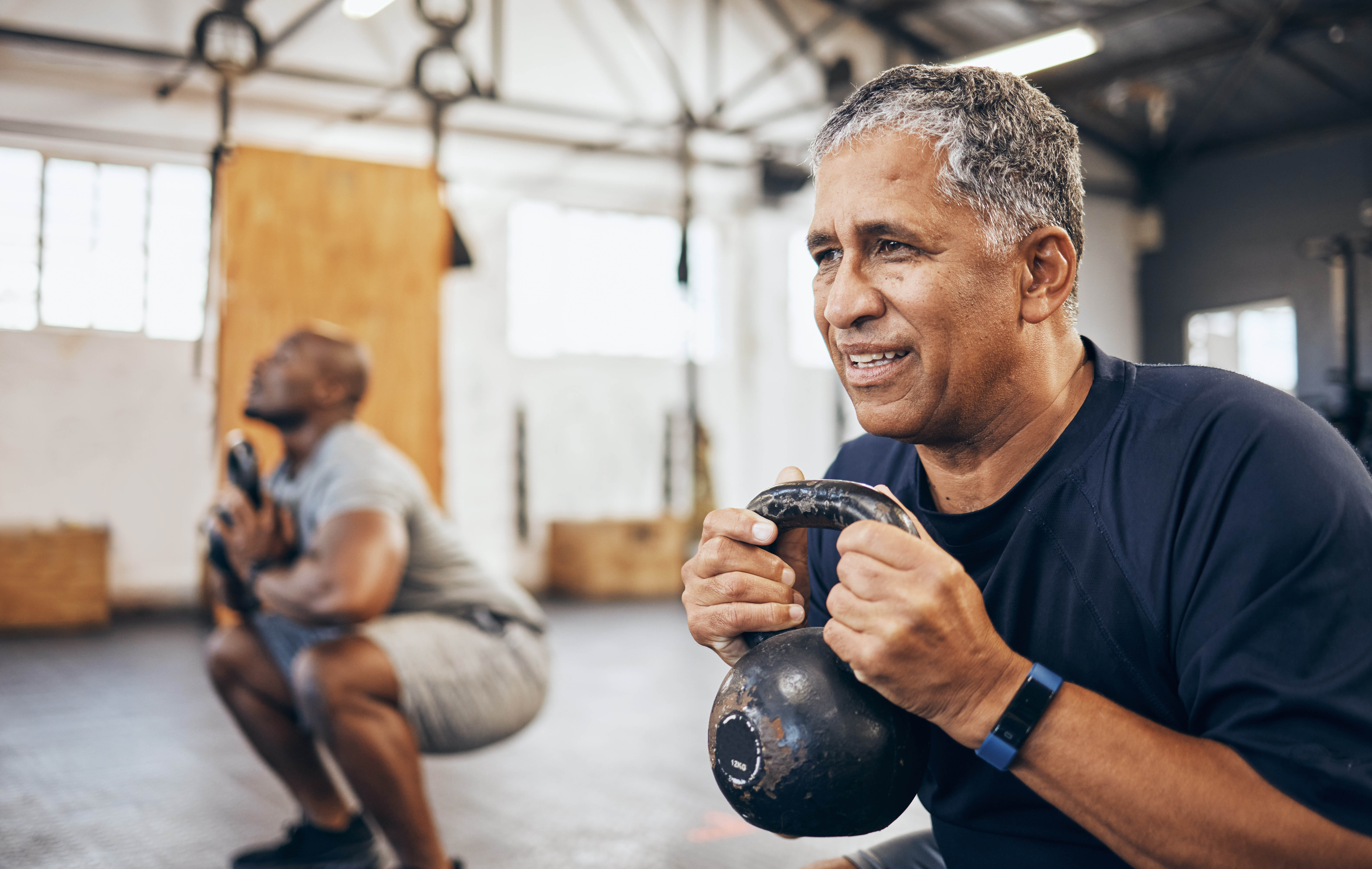 Aging man struggling to complete kettlebell squats in a workout class at the gym